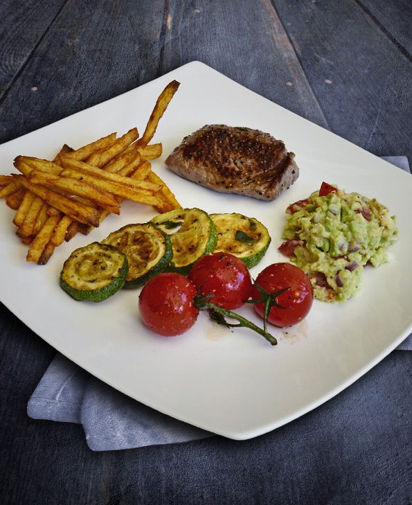 Kleines Steak mit Ofenpommes, Guacamole, Tomaten und Zucchini