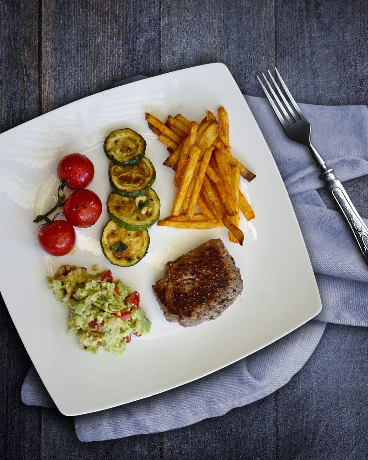 Kleines Steak mit Ofenpommes, Guacamole, Tomaten und Zucchini