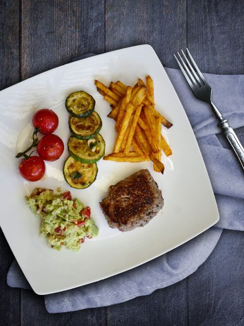 Kleines Steak mit Ofenpommes, Guacamole, Tomaten und Zucchini