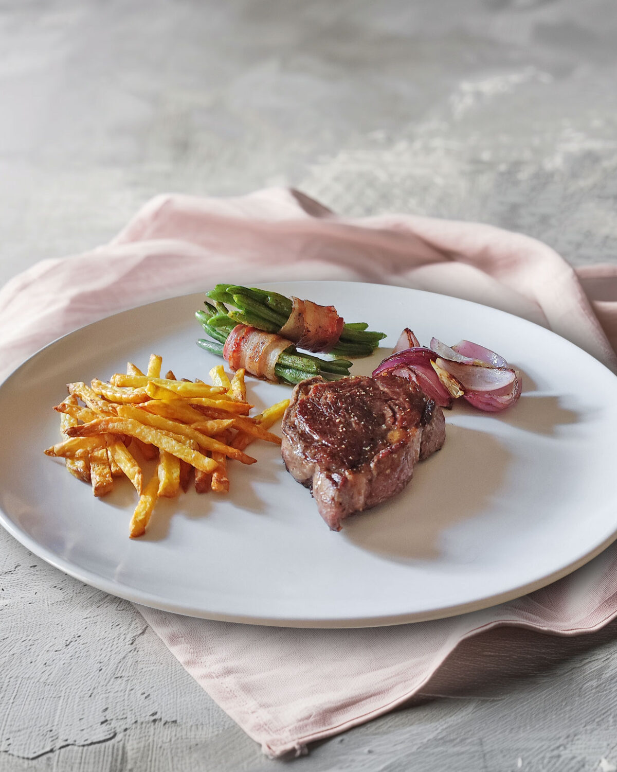 Rib Eye Steak mit Bohnen im Speckmantel, Zwiebeln und Pommes