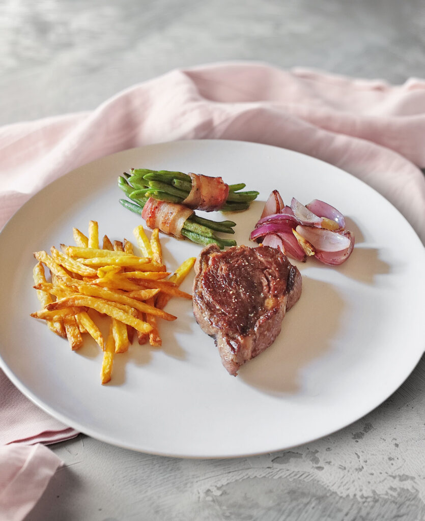 Rib Eye Steak mit Bohnen im Speckmantel, Zwiebeln und Pommes