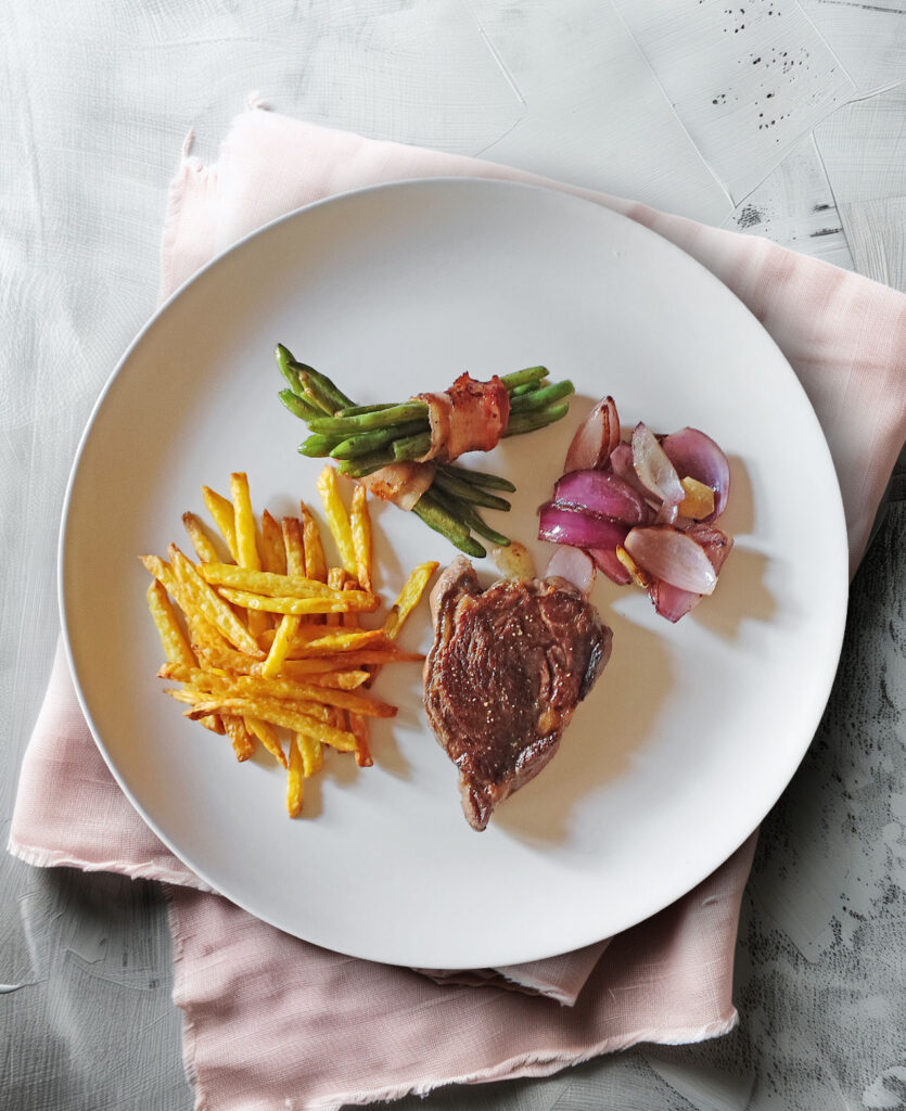 Rib Eye Steak mit Bohnen im Speckmantel, Zwiebeln und Pommes